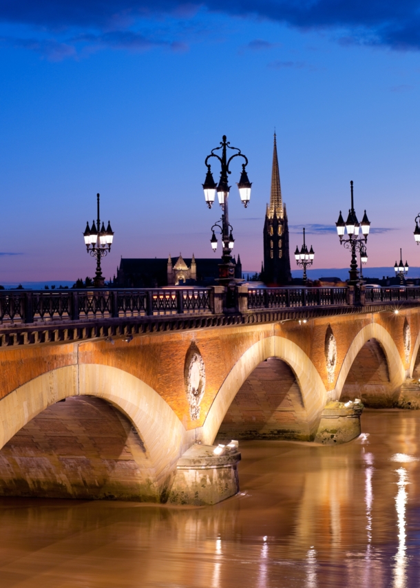 Eine alte Steinbrücke mit erleuchteten Straßenlaternen verläuft über einen Fluss in Bordeaux bei Nacht