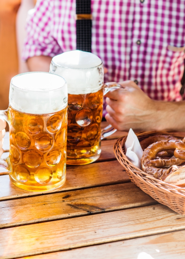 Nahaufnahme von zwei Männern, die an einem Tisch in einem Brauhaus mit zwei Maßkrügen Bier anstoßen