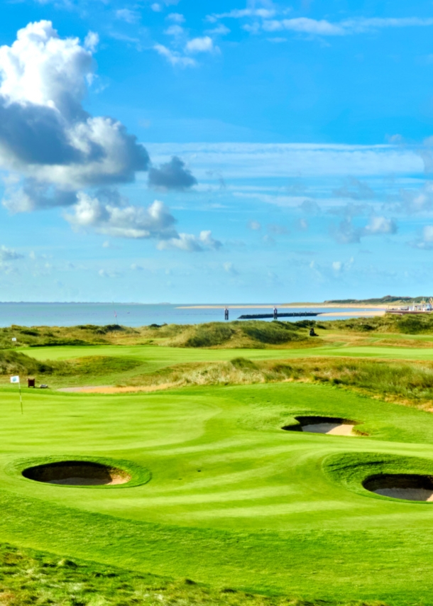 Grüner Golfplatz mit runden Bunkern mit Hotel und Meer im Hintergrund