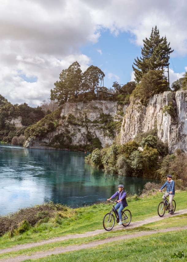 Ein Paar auf Fahrrädern fährt auf einem Radweg entlang eines Sees, umgeben von bewaldeten Felsen