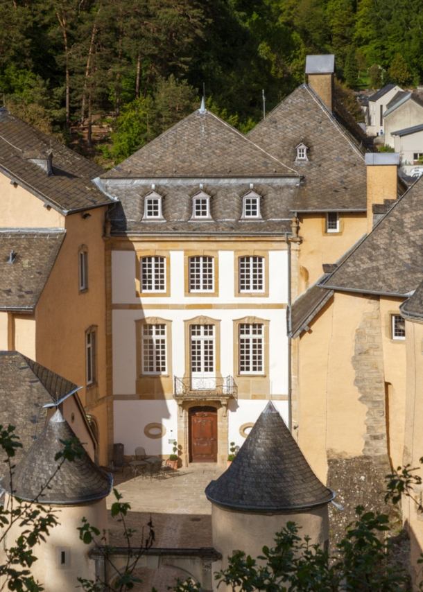 Kleine Burg aus beigem Sandstein mit Rundtürmen und Innenhof in einem bewaldeten Gebiet