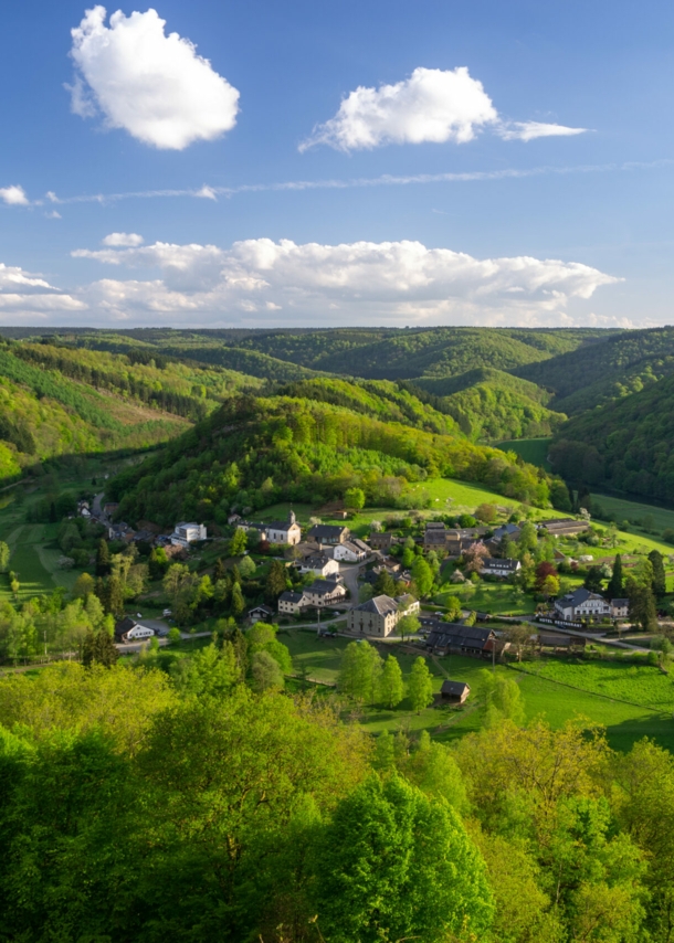 Kleine Ortschaft in einem Flusstal, weitläufig umgeben von hügeliger Waldlandschaft