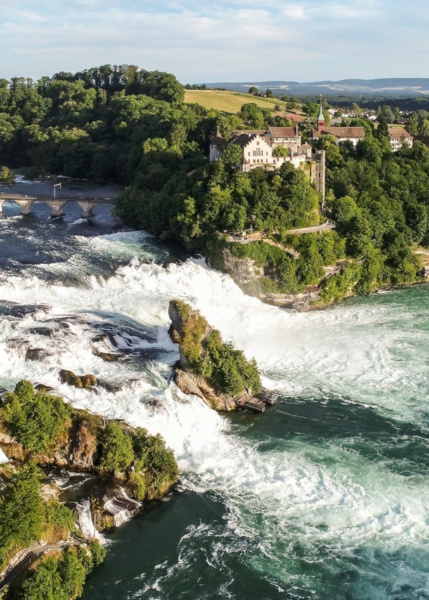 Luftaufnahme des Rheinfalls mit Schloss Laufen inmitten bewaldeter Natur