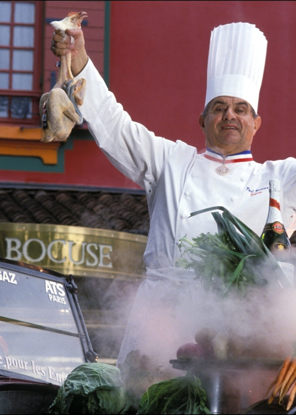 Paul Bocuse in Kochuniform bei einer Inszenierung mit Lebensmitteln vor seinem Restaurant