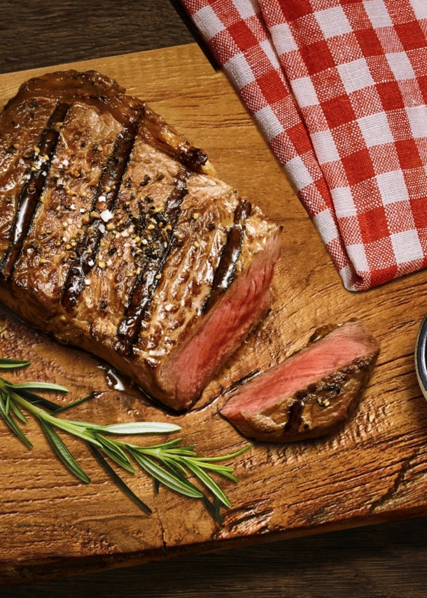 Aufsicht eines gebratenen, angeschnittenen Steaks auf einem Brett neben einer Schale mit Senf.