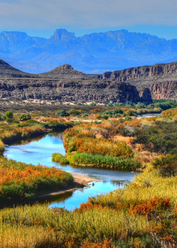 Landschaftspanorama im Big Bend Nationalpark mit mäanderndem Fluss in einer herbstlich gefärbten Graslandschaft vor zwei Gebirgsketten.