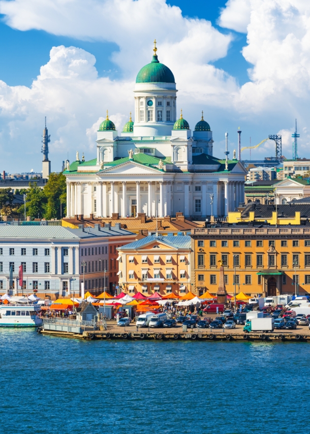 Blick auf eine Stadt am Wasser mit bunten Häusern und einer weißen Kathedrale im Mittelpunkt.