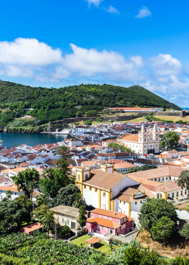 Mediterrane Kleinstadt am Meer, umgeben von grüner Hügellandschaft.