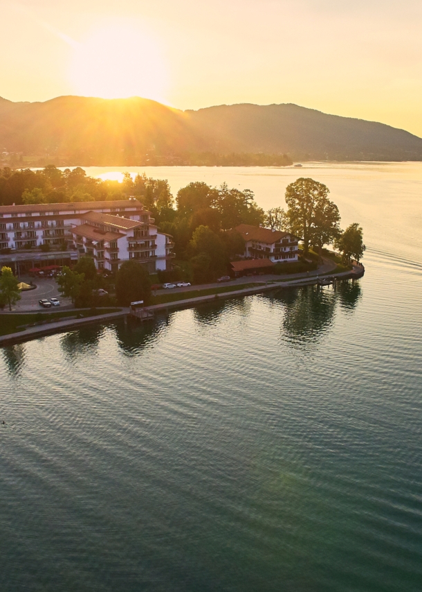 Luxuriöser Hotelkomplex an einem Seeufer, umgeben von Bäumen vor einer bewaldeten Hügellandschaft.