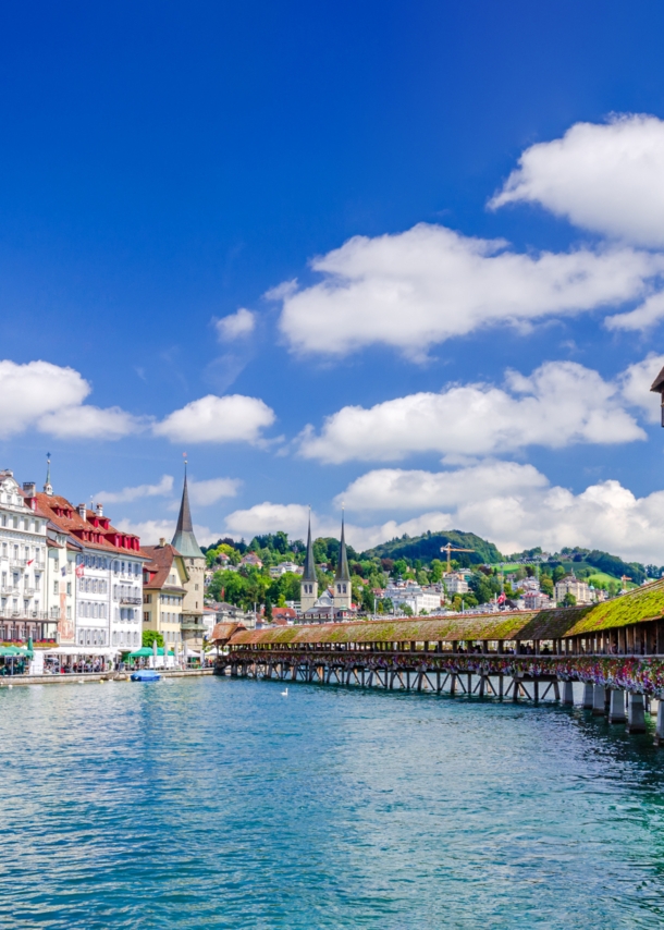 Altstadtpanorama von Luzern am Wasser mit einer hölzernen Brücke vor einem Wasserturm.