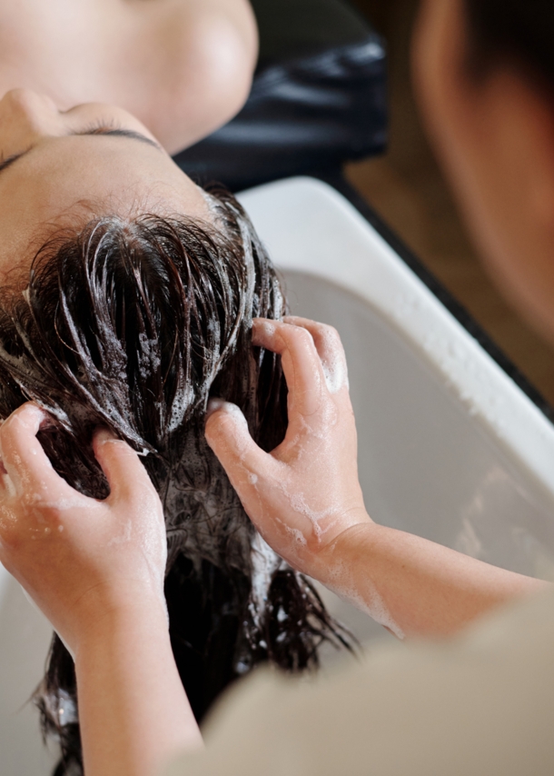 Die Haare einer liegenden Frau werden an einem Waschbecken von einer anderen Person gewaschen.