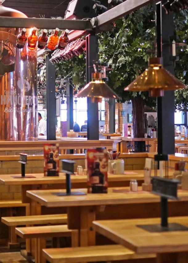 Gastronomiebereich in einem Brauhaus mit Holztischen und großem Kupferkessel.