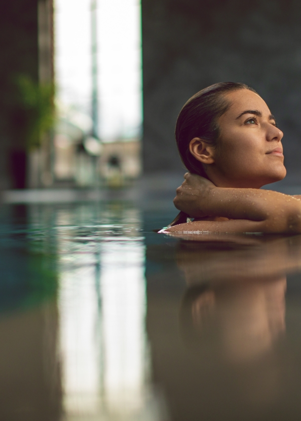 Eine junge Frau entspannt am Beckenrand eines Pools in einem Wellnessbereich.