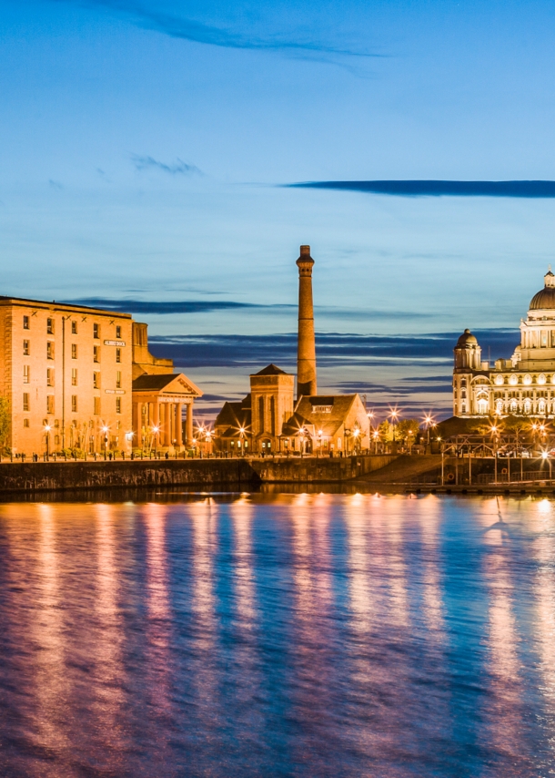 Waterfront in Liverpool bei Nacht mit beleuchteten Gebäuden im Hintergrund.