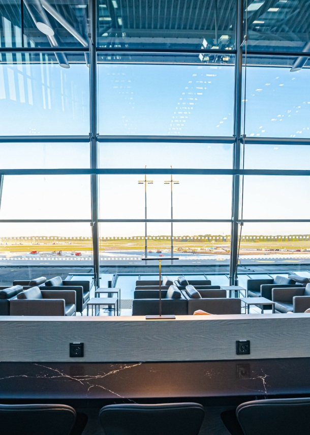 Leere Flughafen-Lounge mit Sitzmöbeln vor Panoramafenstern mit Blick aufs Rollfeld.