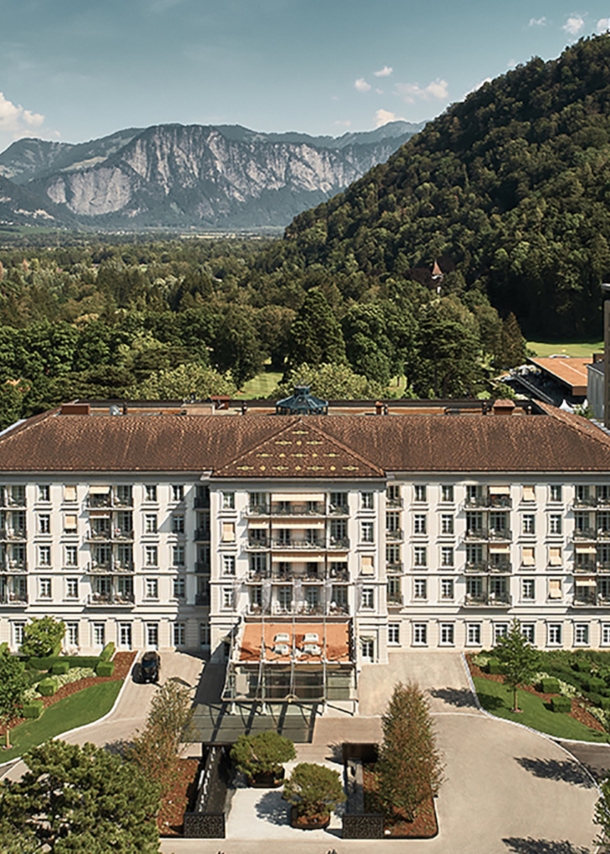 Luftansicht des Grand Resort Bad Ragaz in der Schweiz umgeben von grüner und waldiger Landschaft. Im Hintergrund Berge.