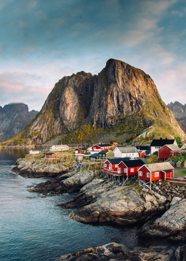 Luftansicht eines Fjords auf den Lofoten mit Felsen, roten Fischerhütten und Bergen.