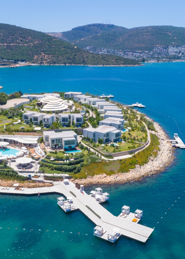 Luftaufnahme eines luxuriösen Hotelresorts mit weißen Bungalows auf einer Landzunge, umgeben von blauem Meer.