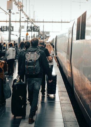 Reisende mit Gepäck laufen am Gleis in einem großen Bahnhof