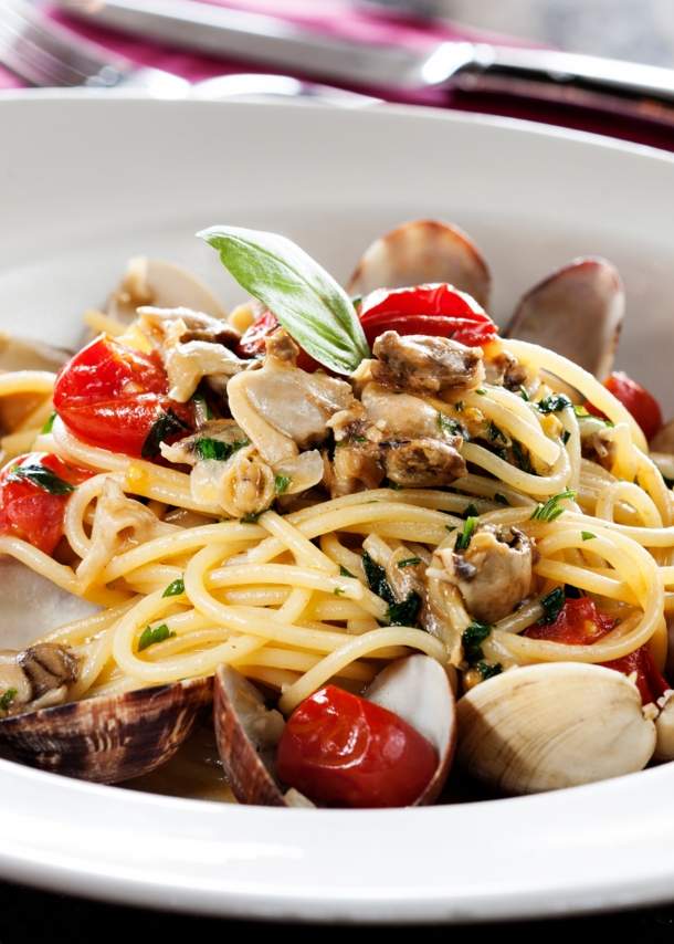 Nahaufnahme einer Portion Spaghetti mit Muscheln und Kirschtomaten auf einem weißen Pastateller.