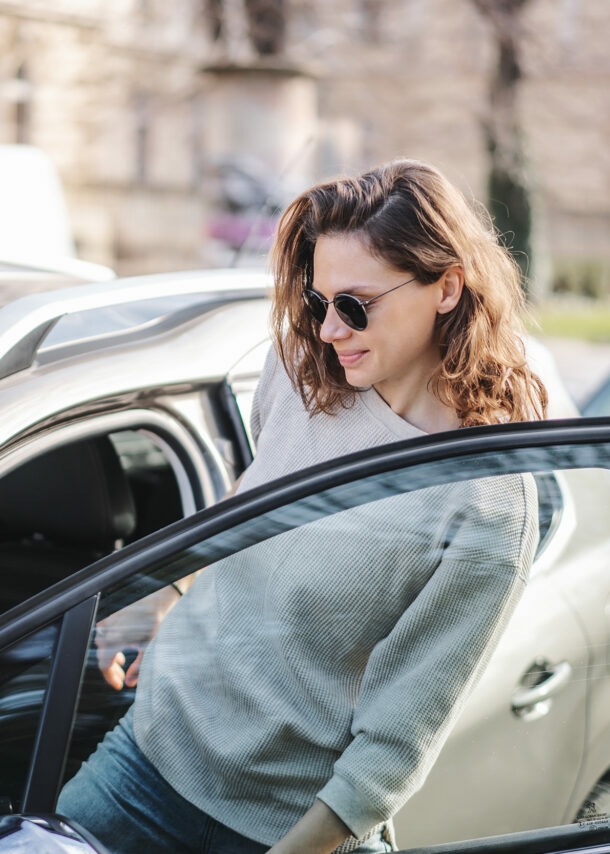 Frau mit Sonnenbrille steigt in parkenden PKW ein