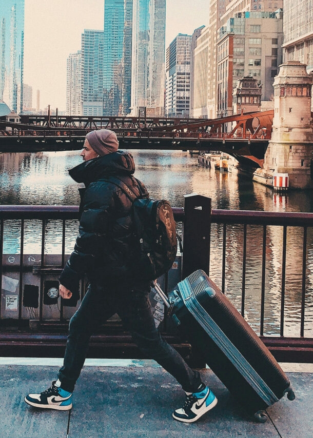 Junger Reisender mit Koffer und Rucksack überquert eine Brücke in Chicago