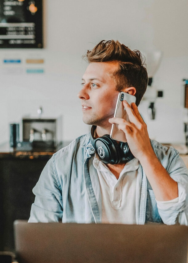 Junger Mann arbeitet im Café am Laptop und telefoniert