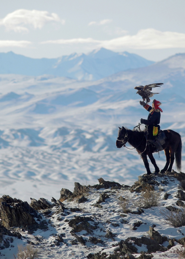 Ein Mann sitzt auf einem Pferd im Gebirge, auf seinem ausgestreckten Arm steht ein Adler.