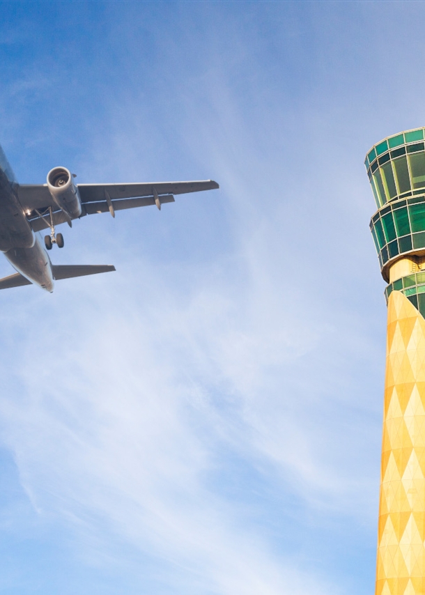 Untersicht eines Flugzeuges am blauen Himmel neben einem grün-gelben Tower. 