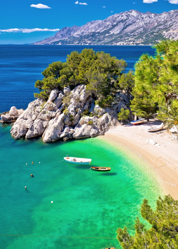 Kleine Sandbucht mit Fischerbooten im türkisblauen Meer, umgeben von Felsen und Kiefernwald.