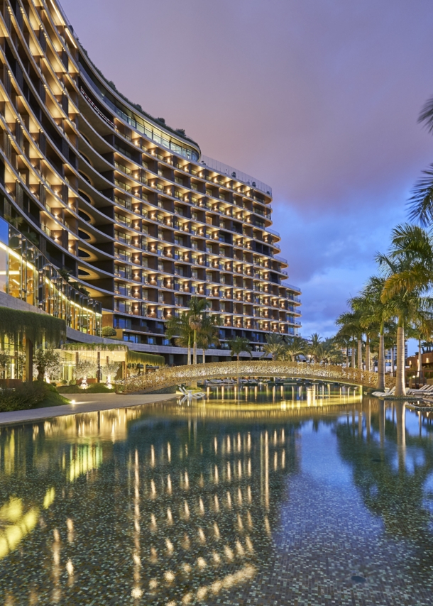 Blick auf ein beleuchtetes Luxushotel mit Palmen und Wasserbecken.