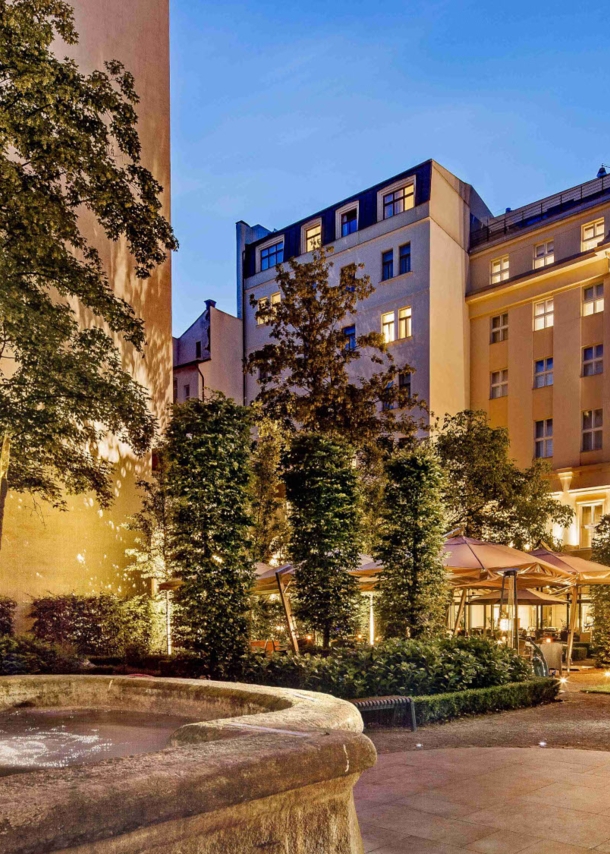 Imposantes, beleuchtetes Hotelgebäude mit barocker Fassade, im Vordergrund ein Springbrunnen mit Löwenkopf.