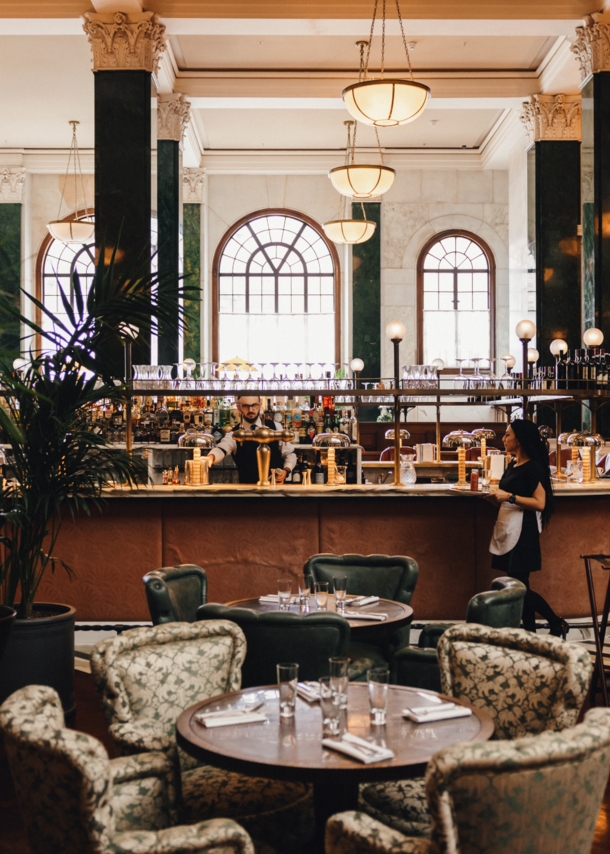 Hotellobby mit grünen Säulen um eine Bar mit Esstischen im 1920er-Jahre-Stil.