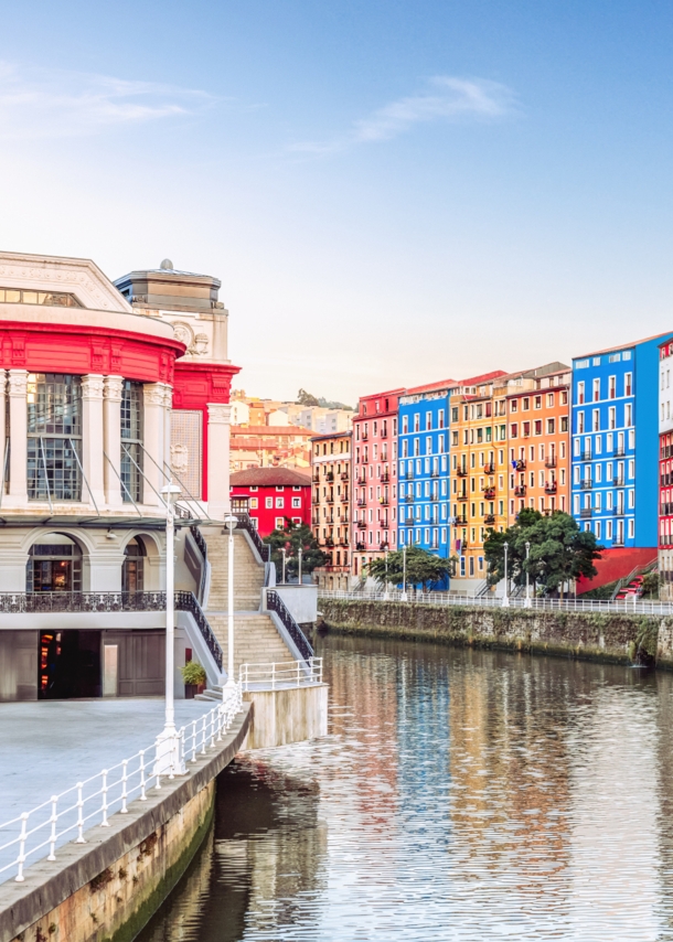 Der Mercado de la Ribera in Bilbao am linken Ufer eines Flusses, auf der anderen Flussseite befinden sich weitere bunte Häuser.