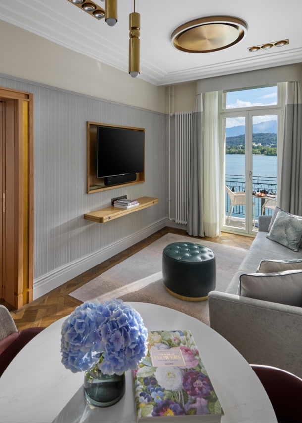 Elegante Hotelsuite mit Balkon an einem See vor Bergpanorama.