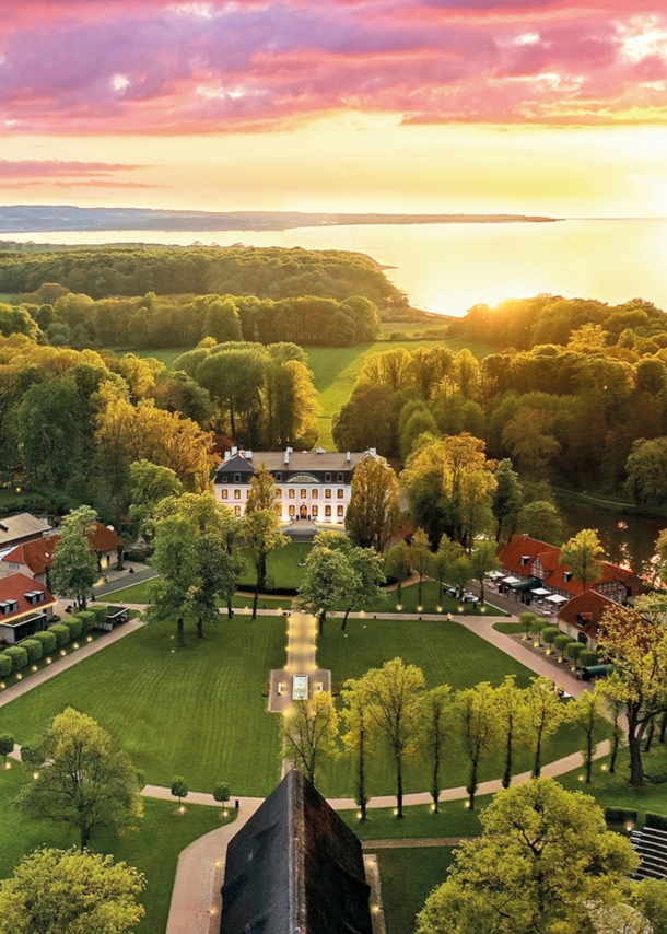 Luxuriöses Hotelresort mit Park- und Waldlandschaft an Meeresküste bei Sonnenuntergang.