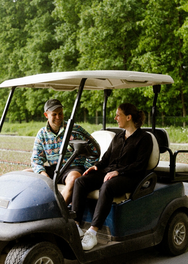 Die Gründerin Antonia Cox sitzt mit Benjamin Diedering in einem Golfplatzfahrzeug und stellt ihm ihr grünes Start-up vor