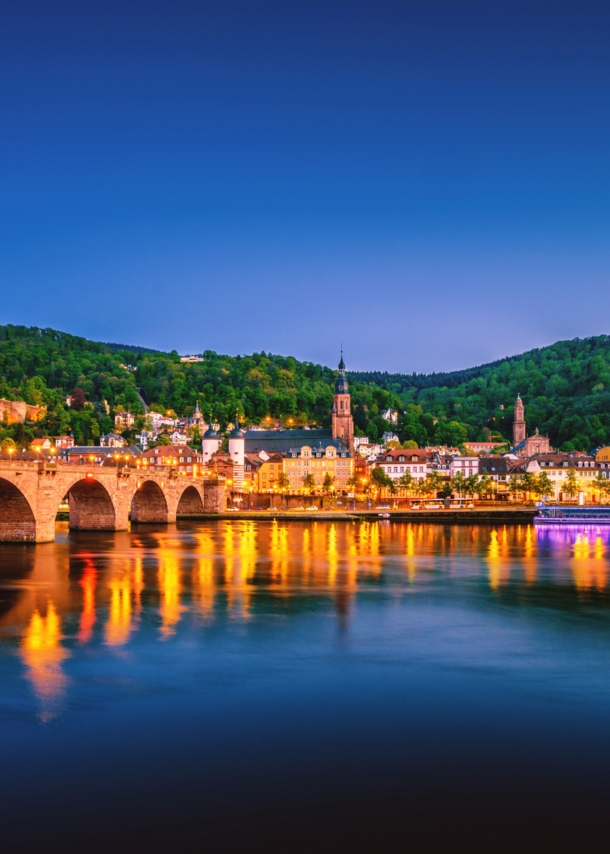 Blick auf die Heidelberger Skyline bei Nacht mit dem Neckar und der Alten Brücke im Vordergrund.