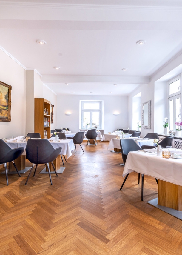 Heller Speisesaal eines gehobenen Restaurants mit Parkett und weiß eingedeckten Tischen.