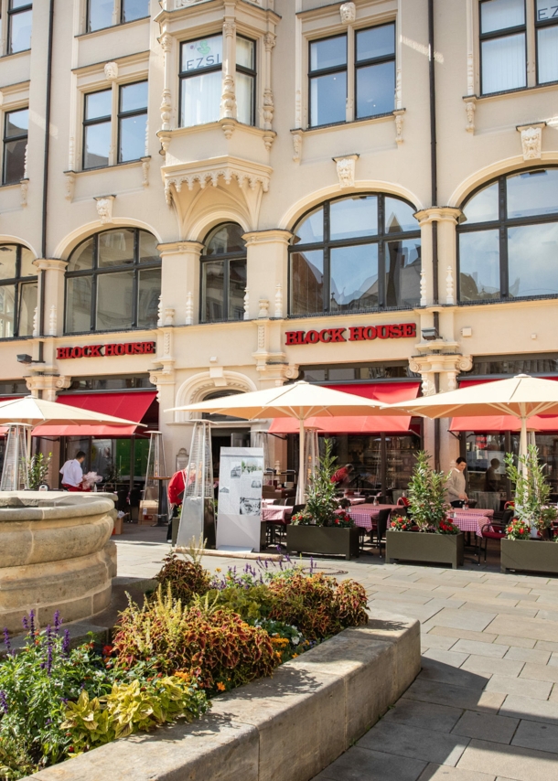 Block House Restaurant mit Außengastronomie in einem historischen Gebäude an einem Platz mit Brunnen in einer Altstadt.