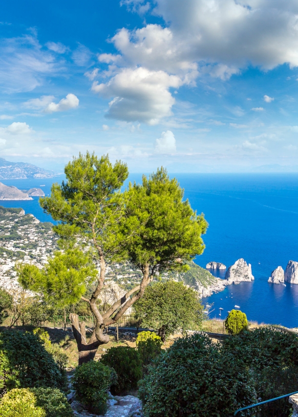 Landschaftspanorama der Insel Capri im blauen Meer, im Vordergrund eine Steinstatue in einem Park.