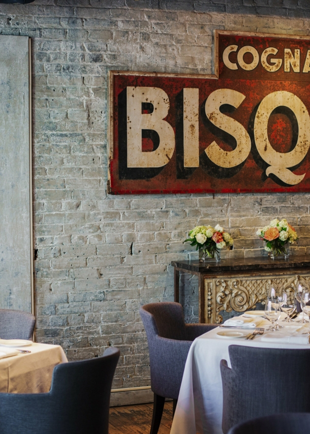 Weiß eingedeckte Restauranttische in einem Raum mit Backsteinwand und antikem Werbeplakat.