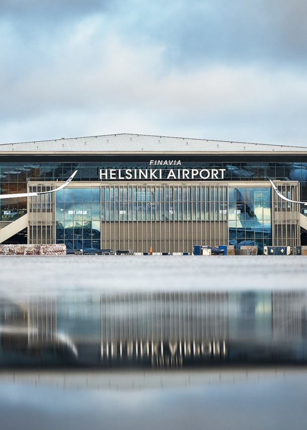 Helsinki Flughafenterminal mit Flugzeugen, im Vordergrund Spiegelung des Gebäudes auf nassem Rollfeld.