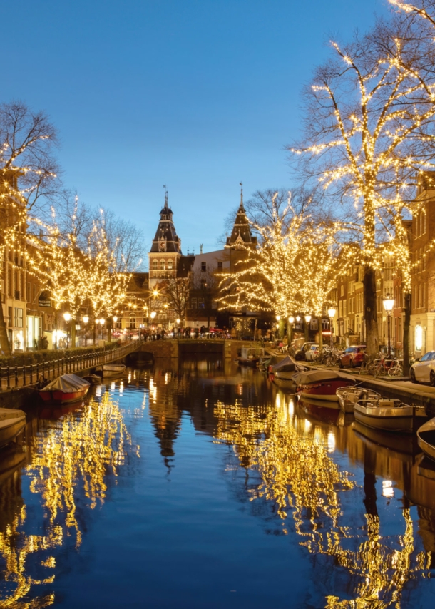 Gracht mit von Lichterketten beleuchteten Bäumen am Abend.