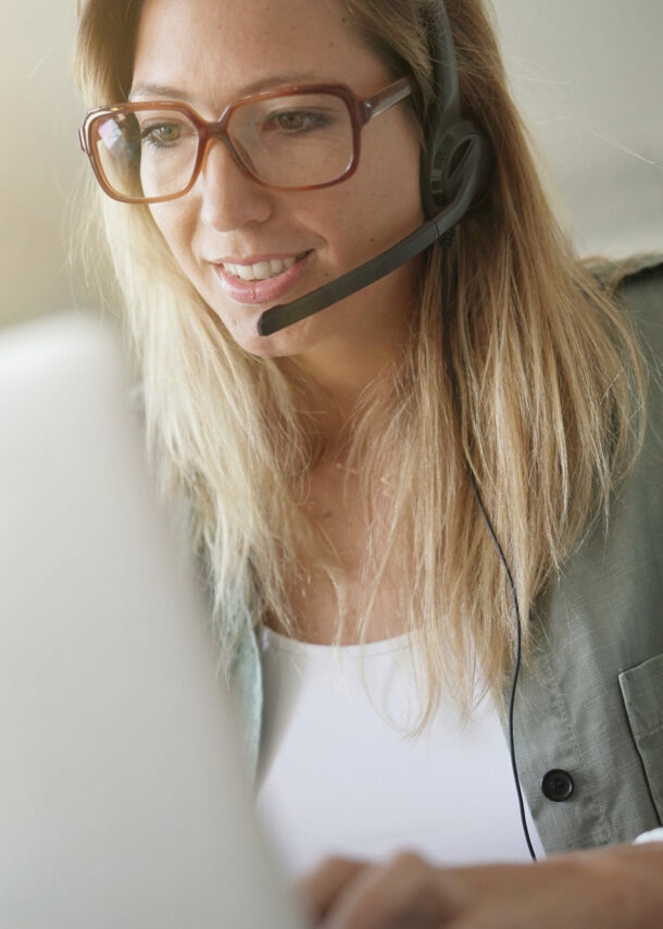 Eine blonde Frau mit Headset sitzt vor einem Laptop und arbeitet.