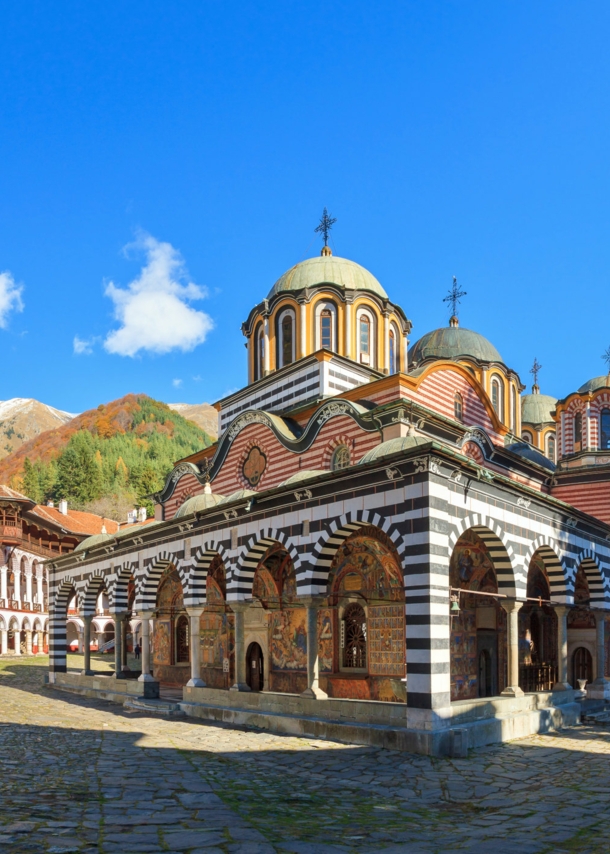 Orthodoxe Klosteranlage mit farbenfrohen Gebäuden im Gebirge unter blauem Himmel.