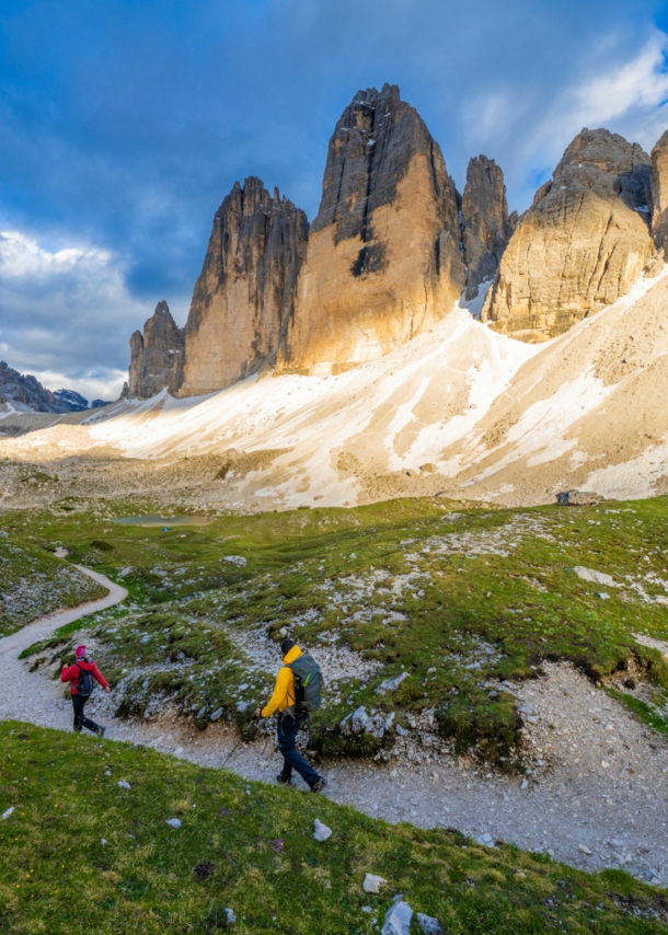 Zwei Personen beim Wandern, im Hintergrund Berge, blauer Himmel und Wolken.