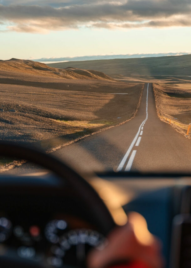 Blick auf eine Landstraße in karger, hügeliger Naturlandschaft durch die Windschutzscheibe eines fahrenden Autos.