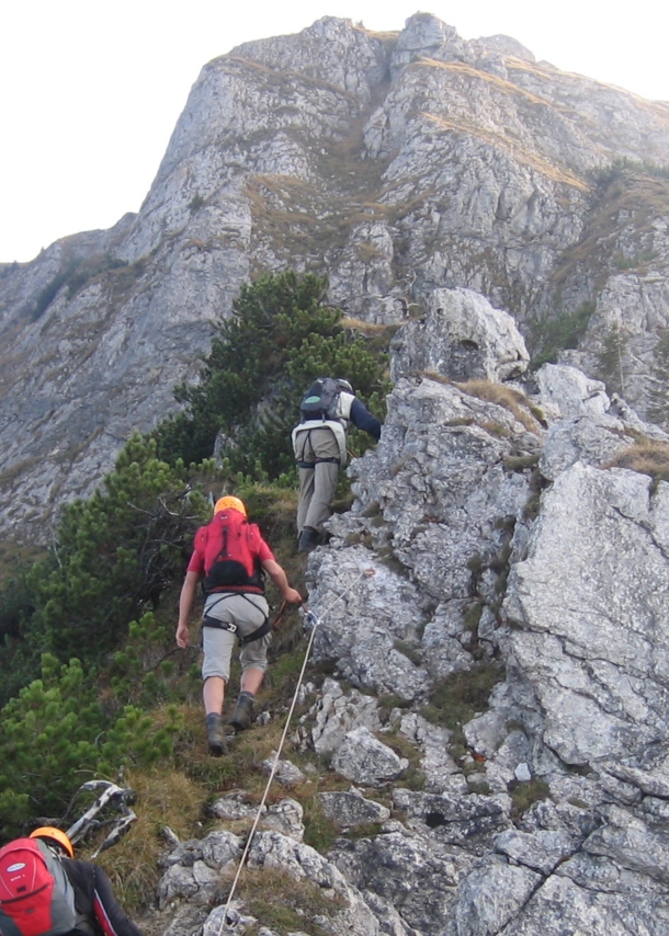 Drei Personen in Kletterausrüstung an einem Felsen an einem der Tegelberger Klettersteige.