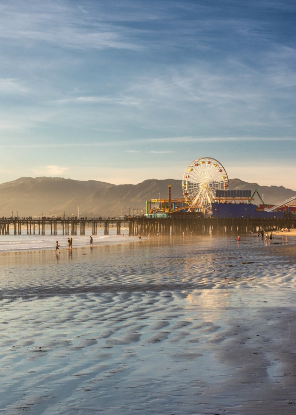 Ein Pier mit Freizeitpark an einem weitläufigen Sandstrand bei Sonnenuntergang.